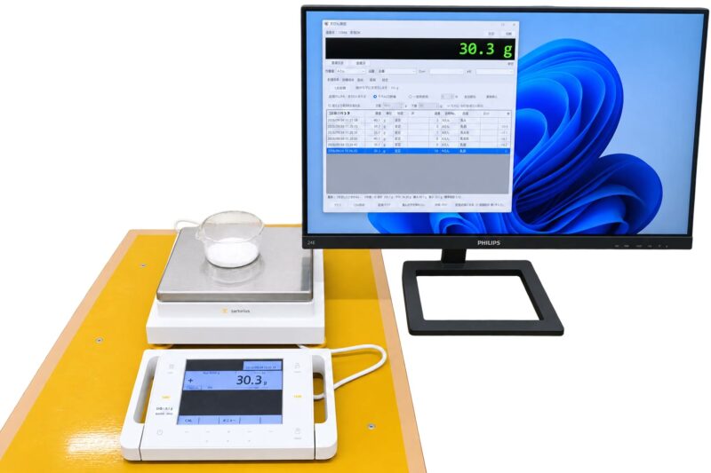 電子天びんとパソコンの画面に計量記録が表示されている様子